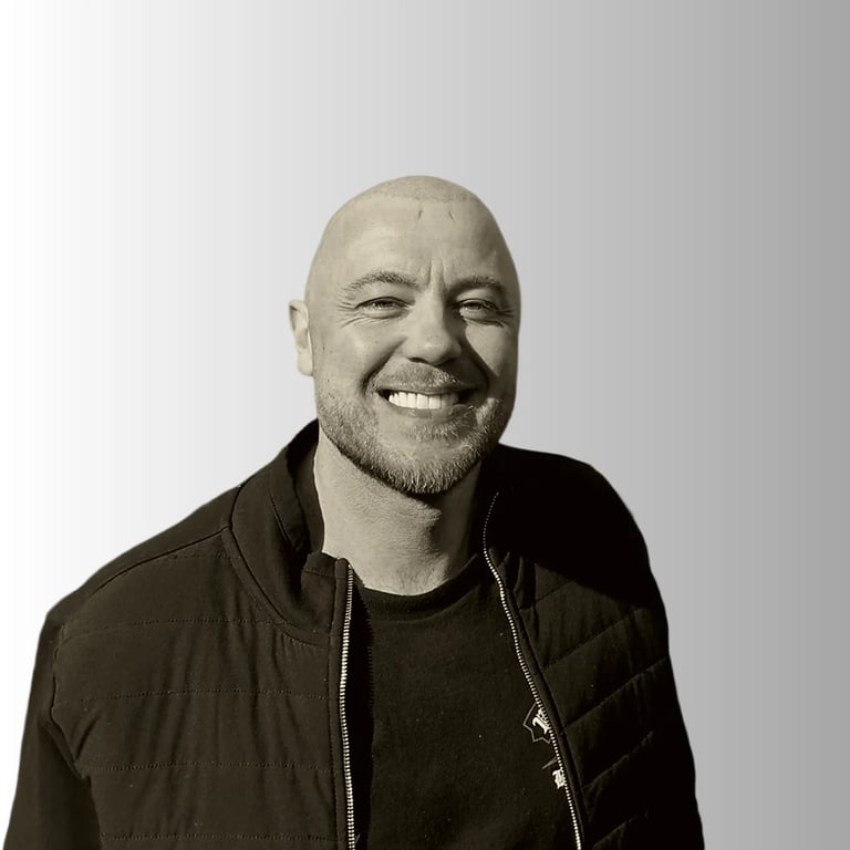 Bald man with beard smiling at camera wearing black jacket over black shirt, studio portrait on white background